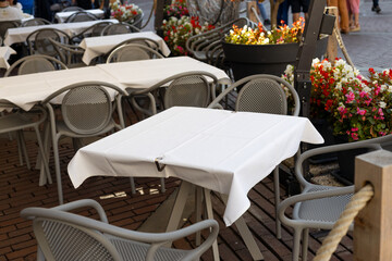 Dining outdoors. Outdoor street cafe tables ready for service. Empty cafe terrace with table and chair. Table of outdoor cafe on sidewalk with colorful plants and flowers
