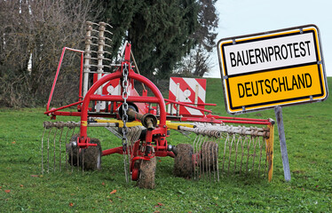Schild mit Bauernprotest Deutschland und einer abgestellten landwirtschaftlichen Maschine auf einem...