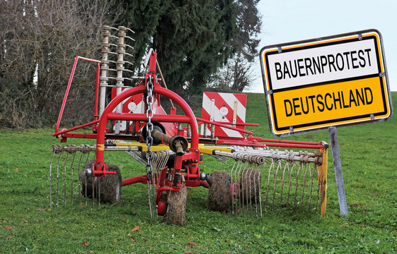 Schild mit Bauernprotest Deutschland und einer abgestellten landwirtschaftlichen Maschine auf einem Feld