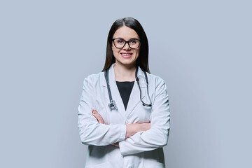 Portrait of confident female doctor in white coat on grey studio background