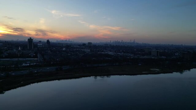 nyc skyline at sunset (aerial drone shot from far away distance in queens) corona flushing meadows park with meadow lake in foreground (setting sun, glow, golden hour) still shot footage