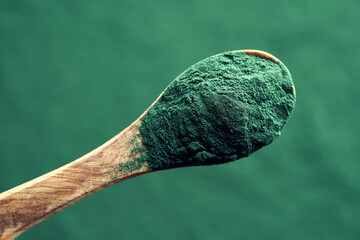 Spirulina powder on a spoon, top view. Nutritional supplement. - obrazy, fototapety, plakaty