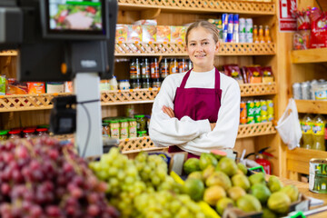 Portrait of smiling young girl wearing apron standing in fruit and vegetable store. First job concept..