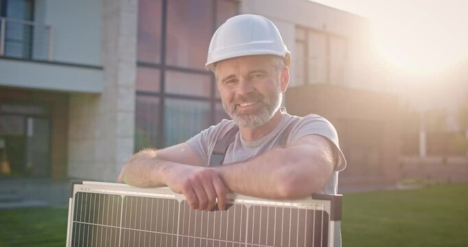 Caucasian man working at renewable energy enterprise. Professional contractor leaning at solar panel and smiling. Male technician engineer installing solar panels. Alternative enersy source.