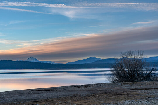 Dramatic image of lake Almanor with Mt Lassen in background and calm reflecting waters and beach in foreground in the California mountains.