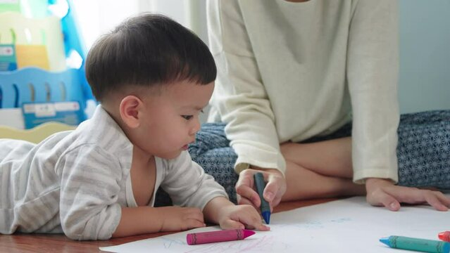 Asian Mother and little son drawing and coloring with Crayons. Woman and little child boy enjoy painting with Crayons on paper together.