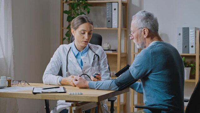 Young female medical worker measuring arterial blood pressure of senior man
