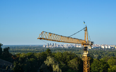 Obraz premium High construction crane with left bank city districts on the background. Urban skyline of Kyiv, Ukraine 