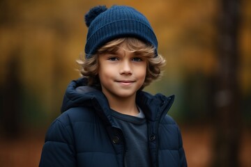 smiling boy in winter jacket and hat standing in autumn forest, portrait
