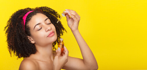 Woman applying skincare product on her face on a yellow background