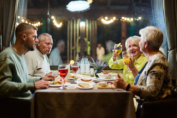 A group of family friends, comprising a young grandson and older individuals, share a delightful dinner in a modern restaurant, exemplifying the concept of healthy aging through intergenerational