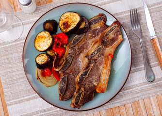 on wooden table plate with grilled beef ribs with fried vegetables-aubergine, pepper,onion.Traditional Spanish dish-churrasco