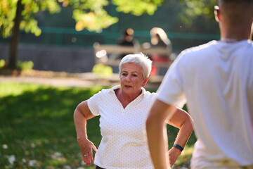 A group of seniors follows a trainer, engaging in outdoor exercises in the park, as they collectively strive to maintain vitality and well-being, embracing an active and health-conscious lifestyle in