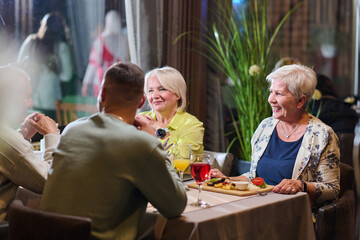 A group of family friends, comprising a young grandson and older individuals, share a delightful dinner in a modern restaurant, exemplifying the concept of healthy aging through intergenerational