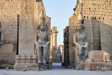 Seated statue of Ramesses II by the Luxor Temple entrance, sunset scenery, Egypt.Luxor Temple main entrance, first pylon with obelisk, Egypt