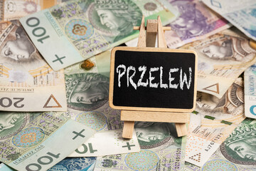 Black writing board on a wooden frame with the inscription "przelew", Polish zloty PLN banknotes scattered in the background (selective focus) translation: transfer