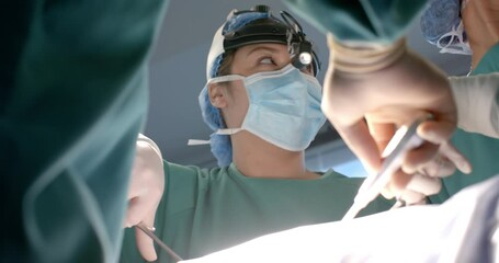 Biracial female surgeon using using headlight and surgical tools during operation, slow motion