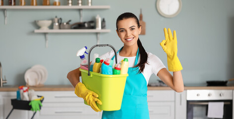 Female janitor with cleaning supplies showing OK in kitchen