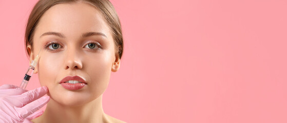 Young woman receiving filler injection in face against pink background with space for text