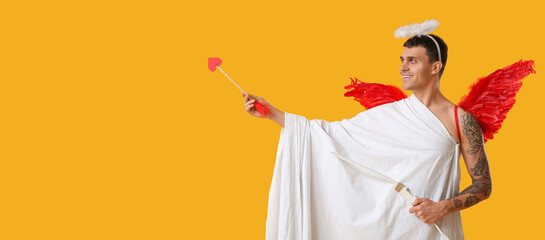 Young man dressed as Cupid with bow and arrow on yellow background with space for text. Valentine's Day celebration