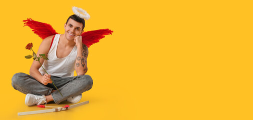 Young man dressed as Cupid with rose on yellow background with space for text. Valentine's Day...