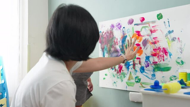 Asian Japanese Mother and little boy make handprints using colorful paints on white paper.