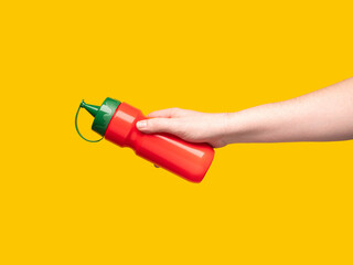 Hand holding a red plastic bottle. Yellow background. 
