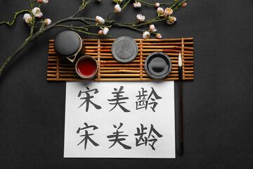 Paper sheet with Asian hieroglyphs, brush, ink, cup of tea and blooming branch on dark background. International Haiku Poetry Day