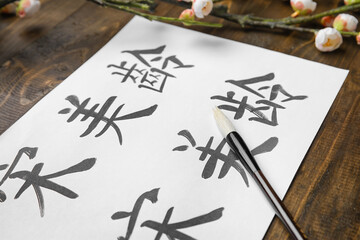 Paper sheet with Asian hieroglyphs and brush on wooden table, closeup. International Haiku Poetry Day