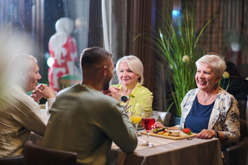 A group of family friends, comprising a young grandson and older individuals, share a delightful dinner in a modern restaurant, exemplifying the concept of healthy aging through intergenerational