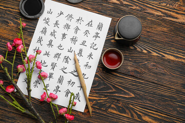 Paper sheet with Asian hieroglyphs, nib pen, ink, cup of tea and blooming branch on wooden background. International Haiku Poetry Day