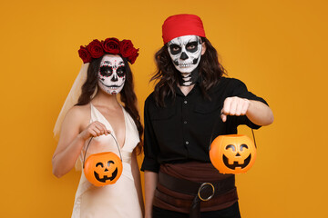 Couple in scary bride and pirate costumes with pumpkin buckets on orange background. Halloween celebration