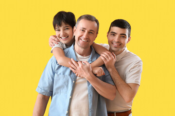 Happy little boy with his dad and grandfather hugging on yellow background