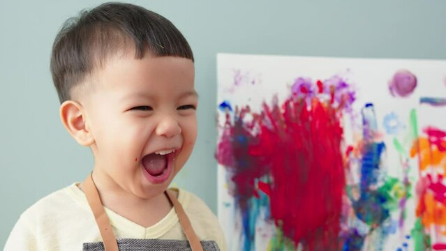 Happy Cute little Asian child boy laughing while painting.
