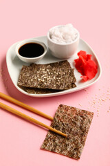 Plate with nori sheets, rice, ginger and soy sauce on color background
