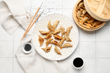 Plate with tasty Chinese jiaozi, sesame and bamboo steamer on white tile background