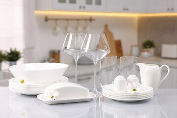 Set of clean dishware, glasses and flowers on table in kitchen