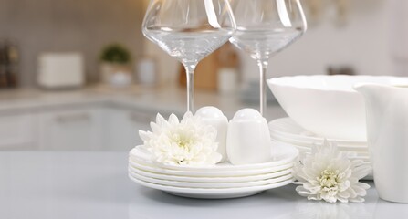 Set of clean dishware, glasses and flowers on table in kitchen. Space for text