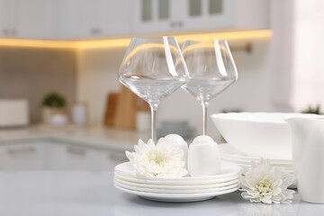 Set of clean dishware, glasses and flowers on table in kitchen. Space for text