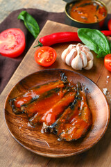 Board with canned fish in tomato sauce and vegetables on wooden table