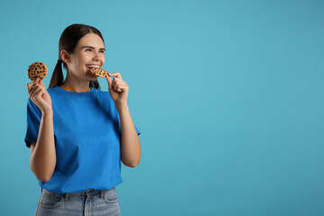 Young woman with chocolate chip cookies on light blue background, space for text