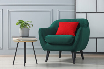 Stylish armchair and side table with houseplant near light grey wall indoors. Interior design