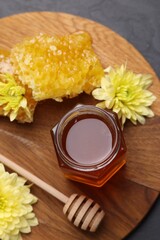 Sweet honey in jar, dipper, chrysanthemum flowers and pieces of honeycomb on grey table, flat lay