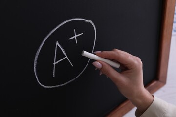 School grade. Teacher writing letter A and plus symbol with chalk on blackboard, closeup