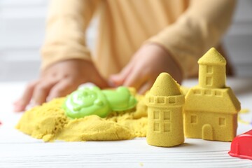 Little child playing with yellow kinetic sand at white wooden table, selective focus