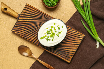 Bowl of tasty sour cream with green onion on beige background