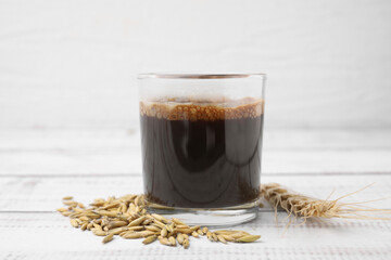 Cup of barley coffee, grains and spike on white wooden table, closeup
