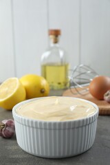 Fresh mayonnaise sauce in bowl and ingredients on grey table