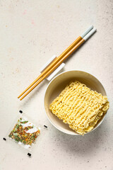 Raw instant noodles in bowl with seasoning and chopsticks on white grunge background