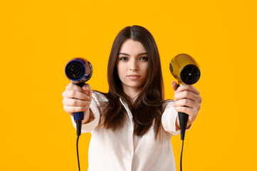Beautiful young woman with hair dryers on yellow background